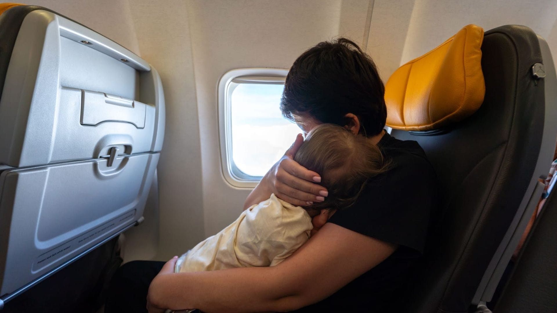 Loving mother holding her precious baby by airplane window during flight