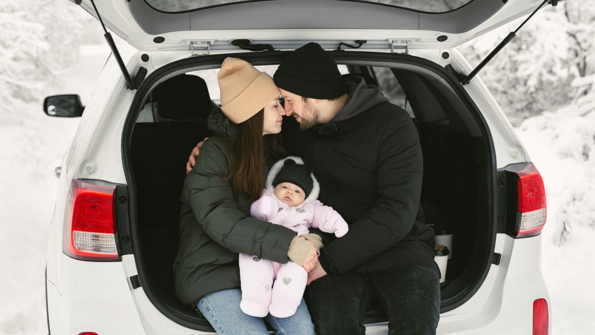 Young-happy-family-a-man-a-woman-and-a-baby-are-sitting-in-the-trunk-of-a-car-in-a-winter-snow-covered-forest