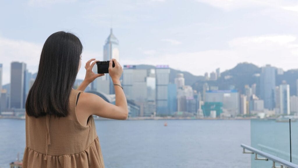 oung-Woman-taking-photo-with-cellphone-in-Hong-Kong-Victoria-harbor
